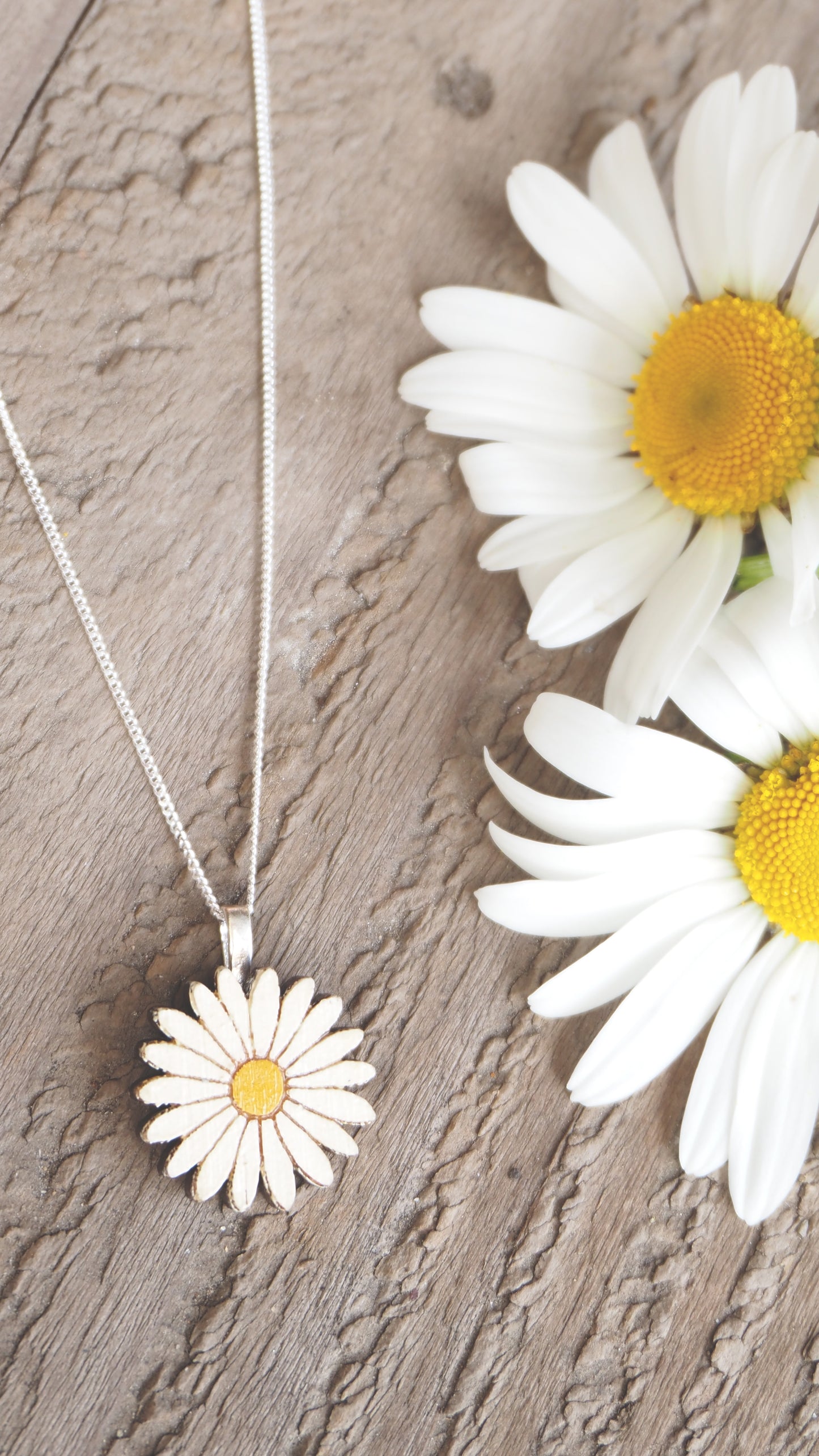 Daisy-shaped pendant necklace on a wooden surface with daisies.