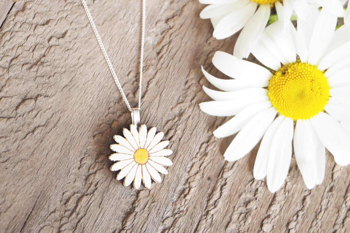 Daisy-shaped necklace on a wooden surface with daisies