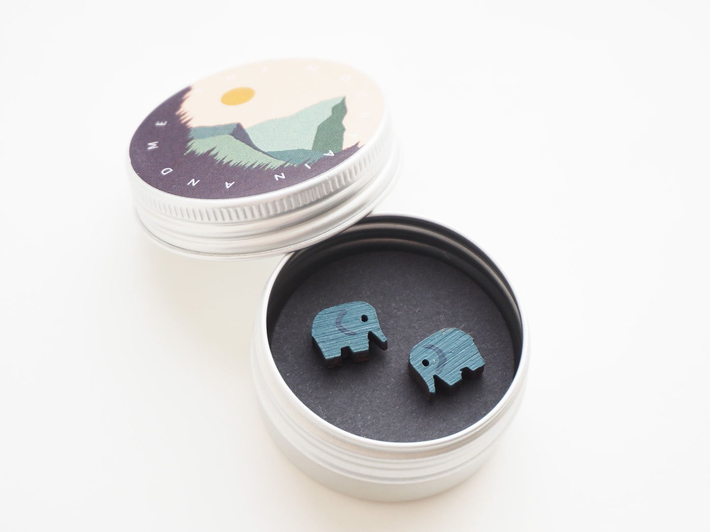 Hand Painted Wooden Elephant Stud Earrings in a tin with mountain design, showcasing blue/grey hand painted elephants.