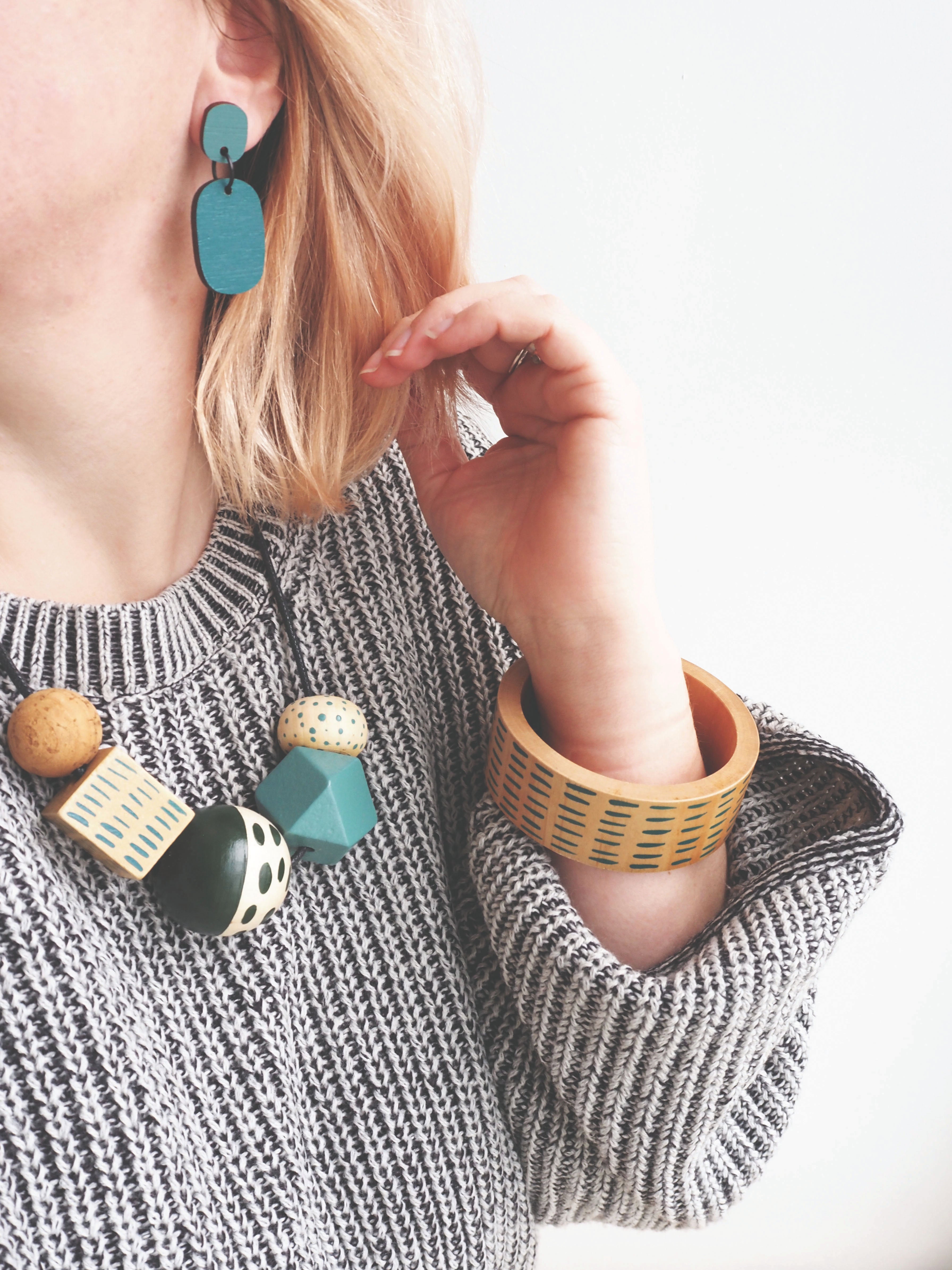 lifestyle photo showing a model wearing a 'The Mountain and Me' wooden necklace, bangle and bamboo earrings all in co-ordinating blue colours.