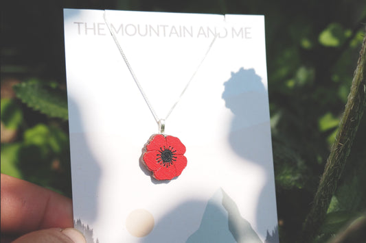 Red poppy necklace on a 'The Mountain and Me' card with a blurred natural background